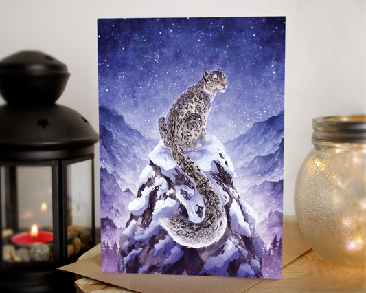 winter greeting card of a snow leopard sat on the peak of a mountain. The snow leopard has snowflakes for the spot patterns, and in the background is a mountain range with a blue starry night sky.